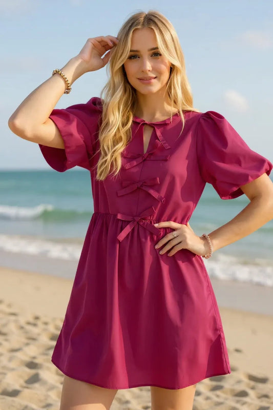 Women's bow detail ruched puff sleeve mini dress front view featuring statement bow at neckline and structured 100 percent cotton fabric