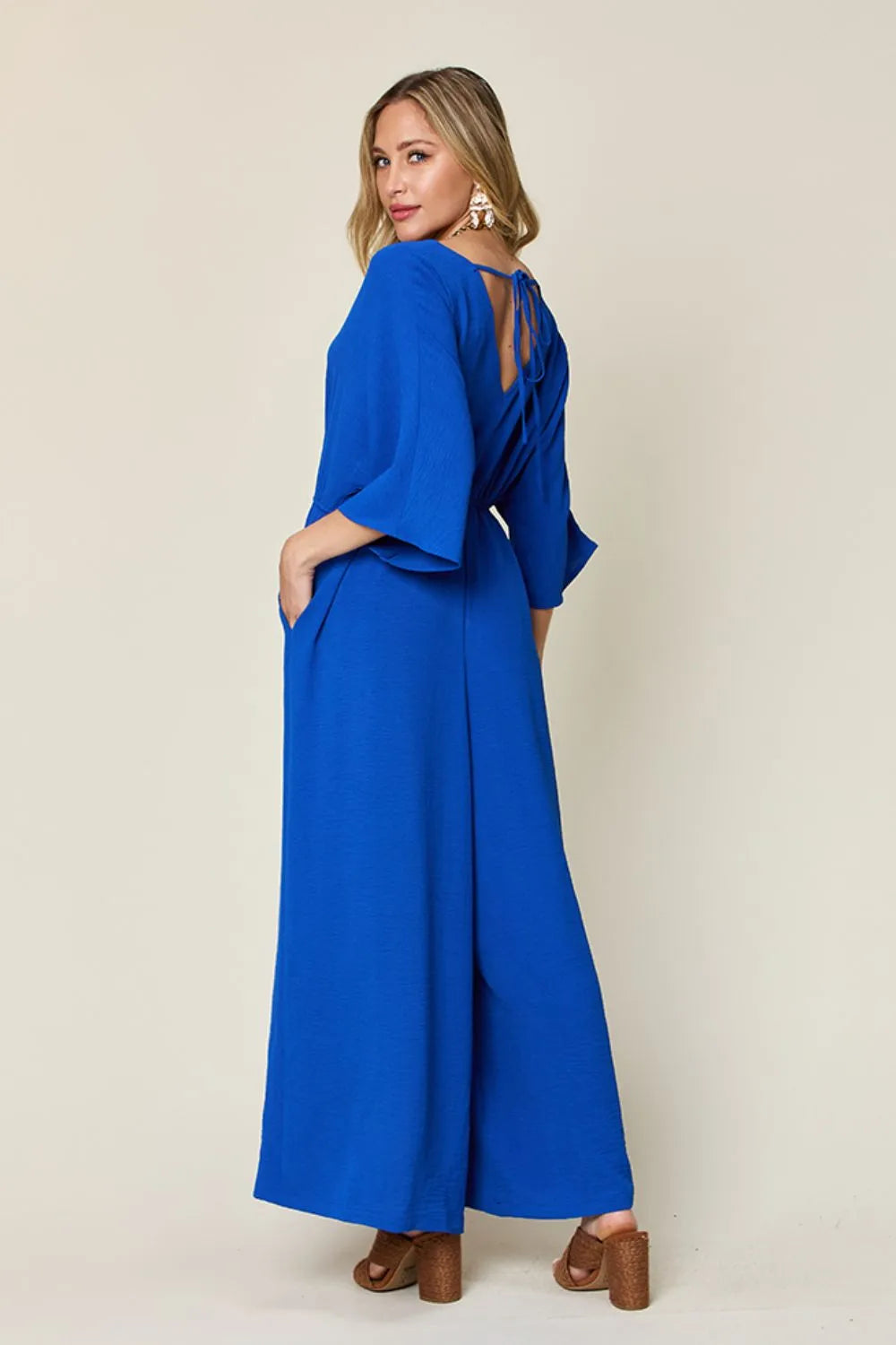 Double Take Full Size Surplice Wide Leg Jumpsuit with Pockets back view model standing, elegant draped back and flowy wide legs