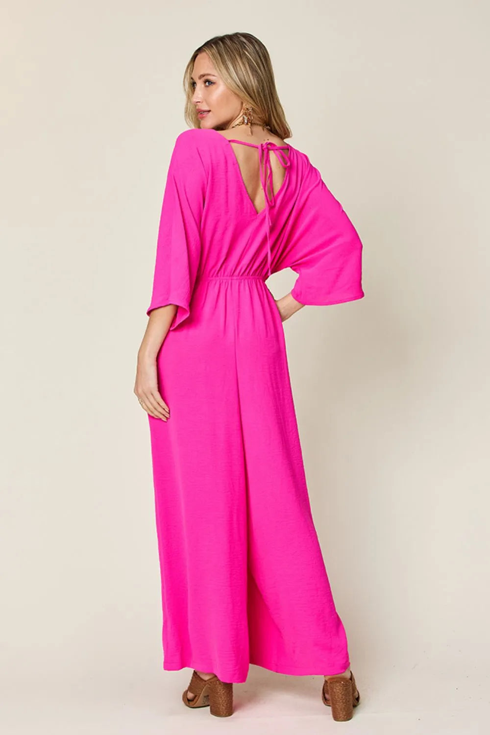 Double Take Full Size Surplice Wide Leg Jumpsuit with Pockets back view model hands in pockets, showing back pockets and flowy wide leg design