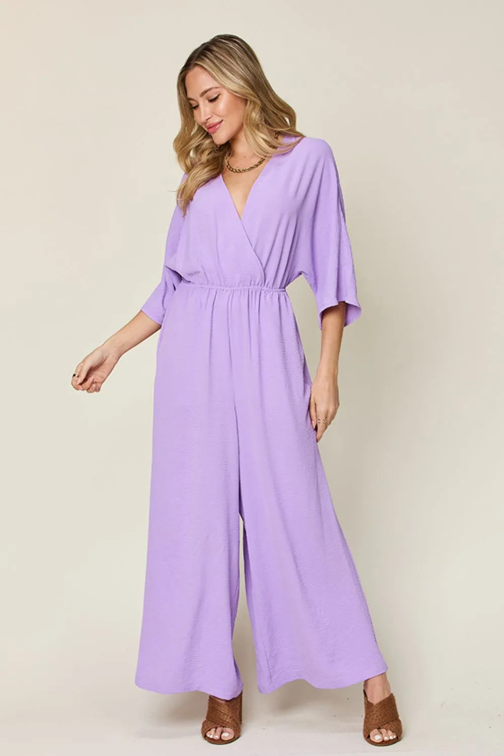 Double Take Full Size Surplice Wide Leg Jumpsuit with Pockets front view model arms out, highlighting draped fabric and elegant design