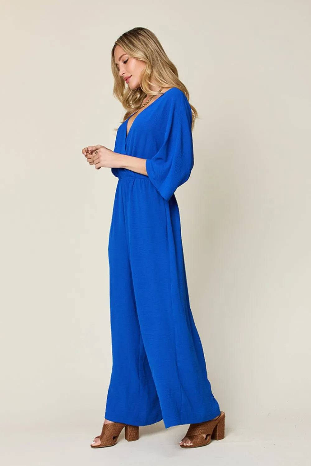 Double Take Full Size Surplice Wide Leg Jumpsuit with Pockets side view model standing, showing wrap silhouette and leg movement