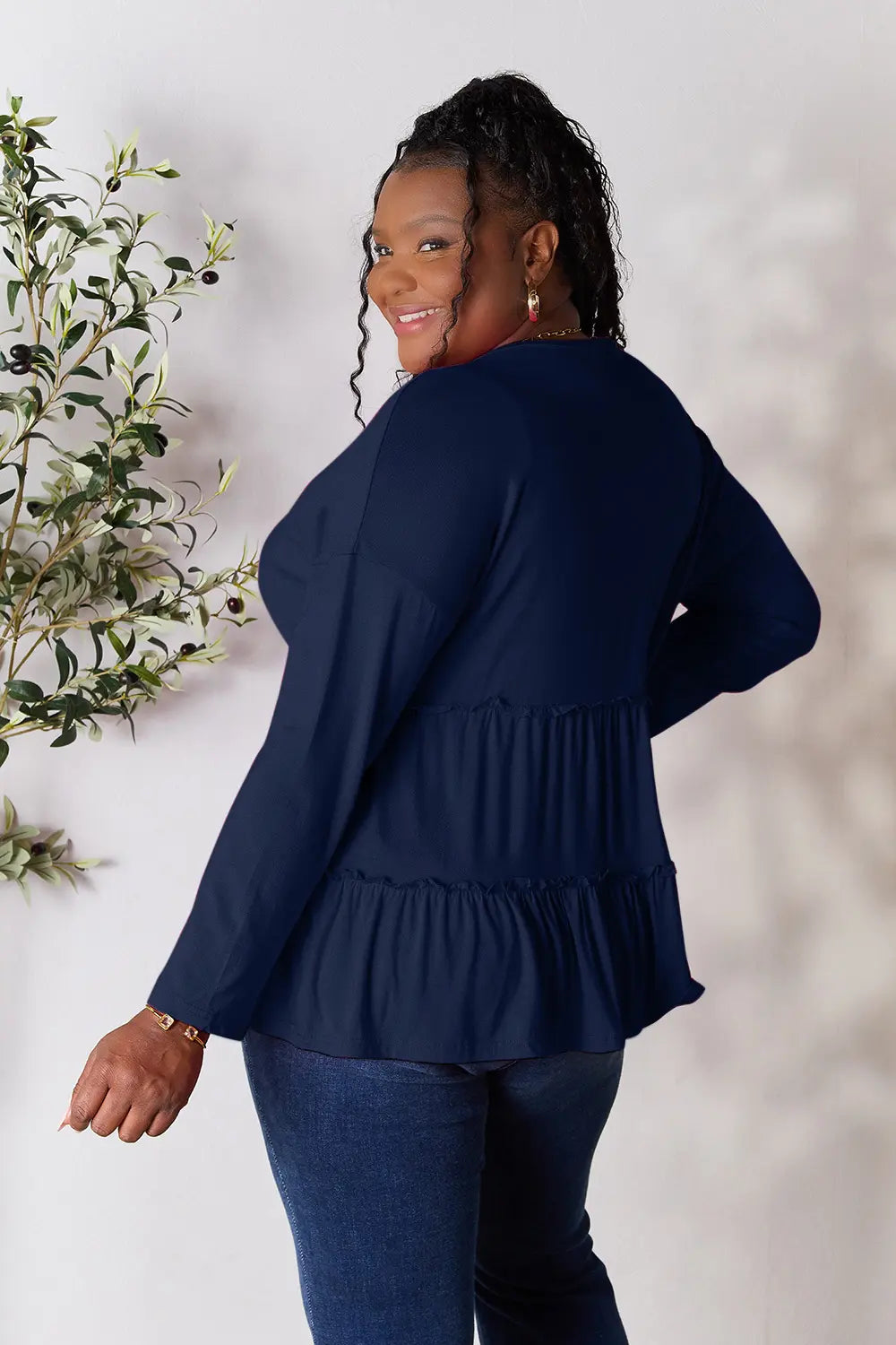 Full-length back view of Double Take half button long sleeve ruffle hem blouse on model.
