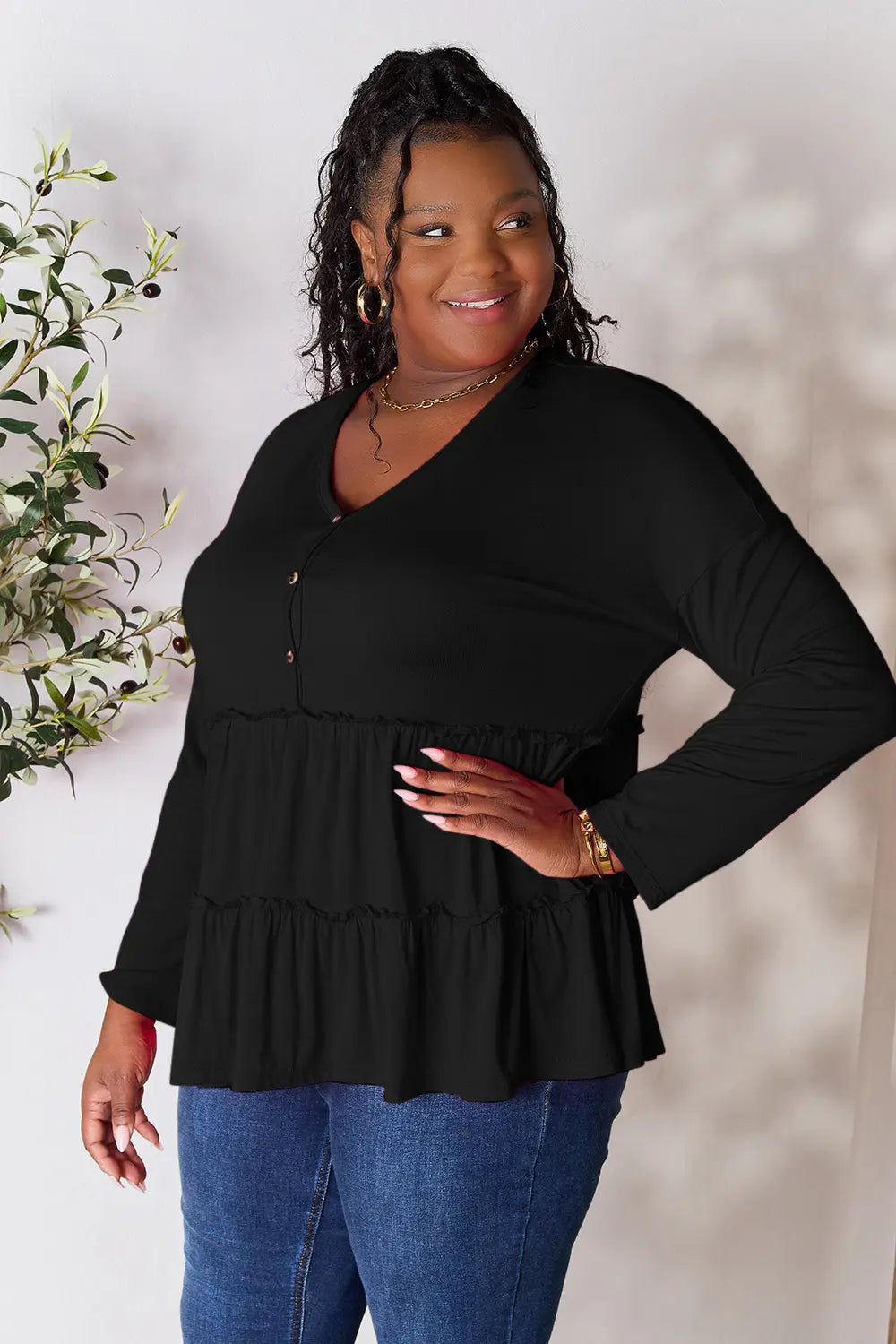 Full-length side view of Double Take half button long sleeve ruffle hem blouse on model.
