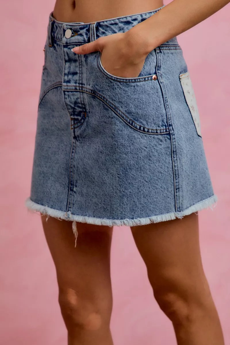 Side view of SO ME washed denim floral mini skirt with floral print, contrast pockets and raw hem, stylish women’s outfit