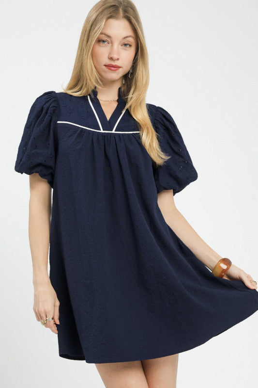 Front view of Umgee puff sleeve textured babydoll dress in navy Swiss dot with V-neck white trim and side pockets.