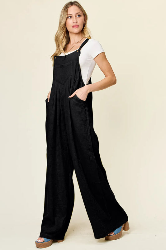 Side profile of woman wearing wide strap overalls, wide leg silhouette flowing from hip, side pocket visible, cotton texture, relaxed one piece outfit